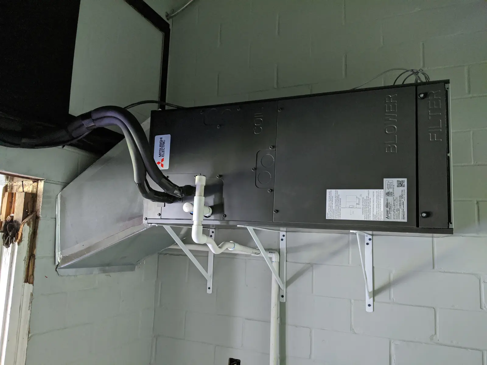 Mitsubishi horizontal ducted air handler mounted on wall brackets with refrigerant lines connected