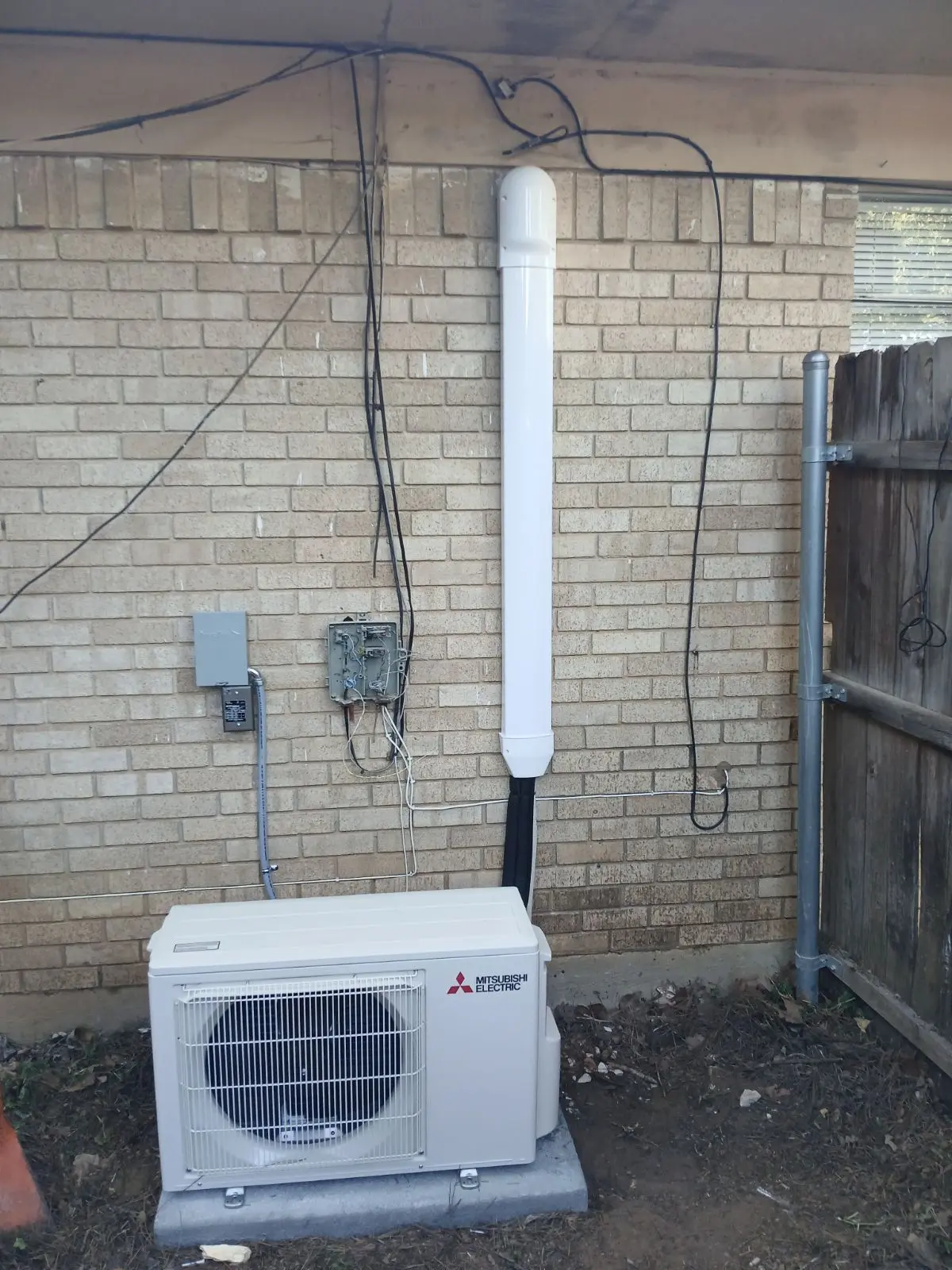 Mitsubishi Electric outdoor unit with a white line hide running up a tan brick wall