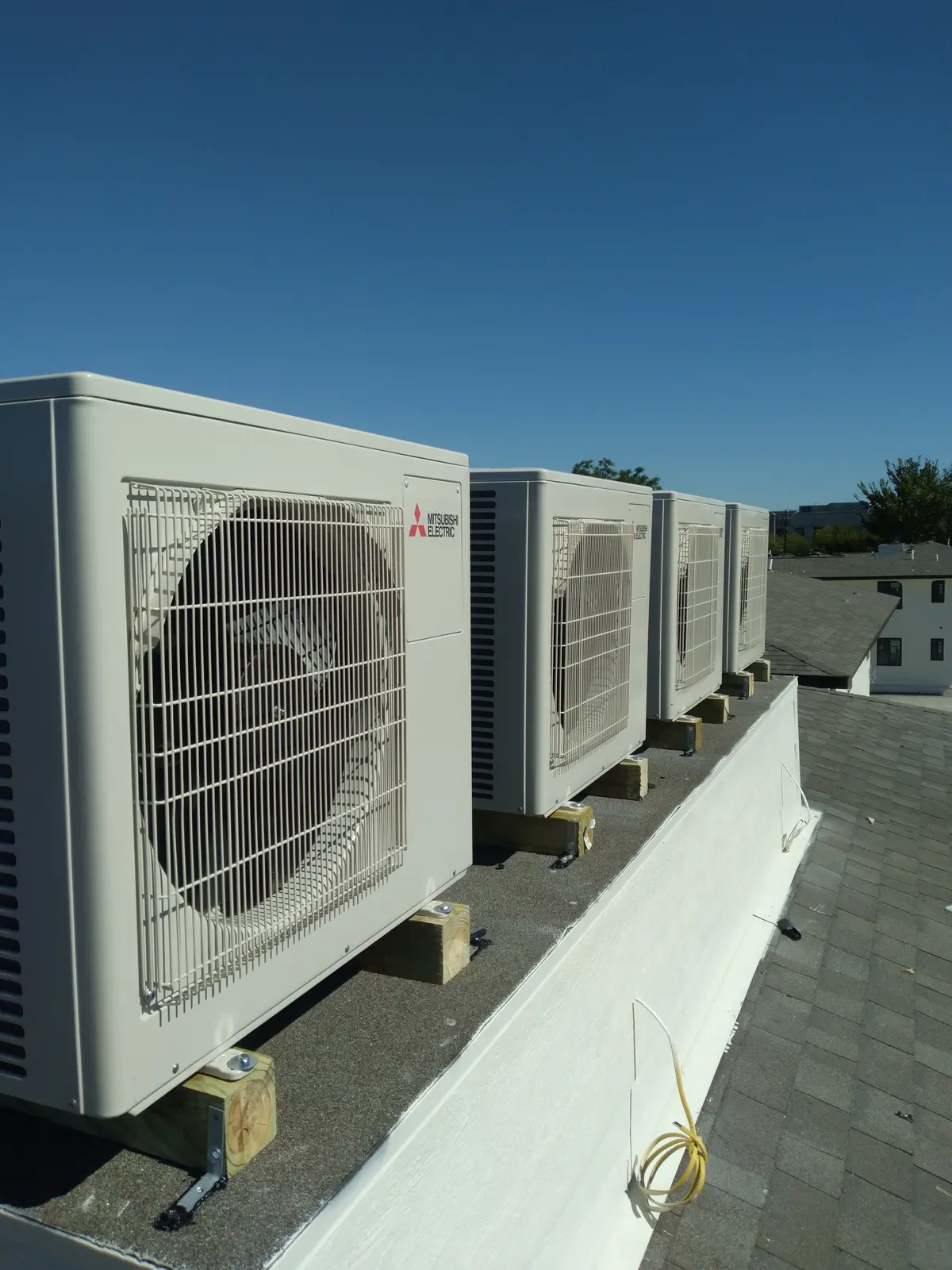 Row of Mitsubishi Electric outdoor units mounted on a commercial rooftop under a clear blue sky