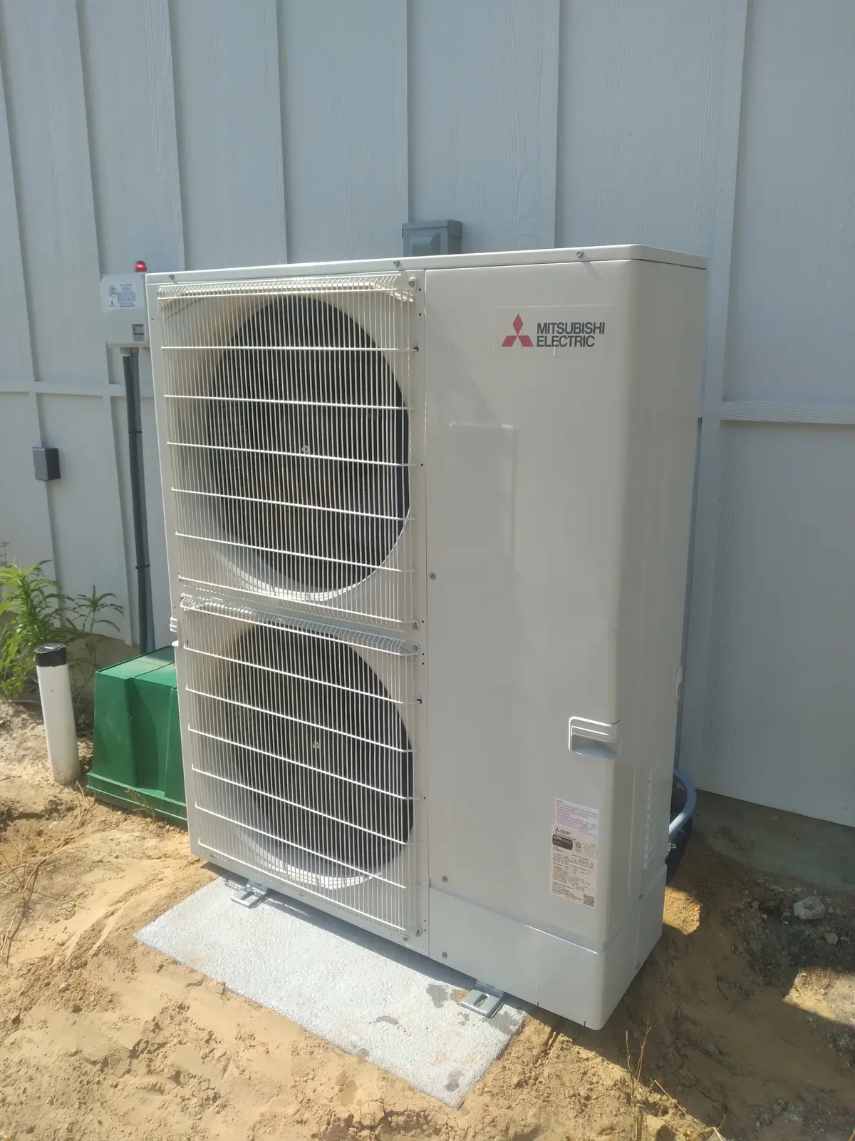 Large Mitsubishi Electric two-fan outdoor unit on a concrete pad beside light gray siding