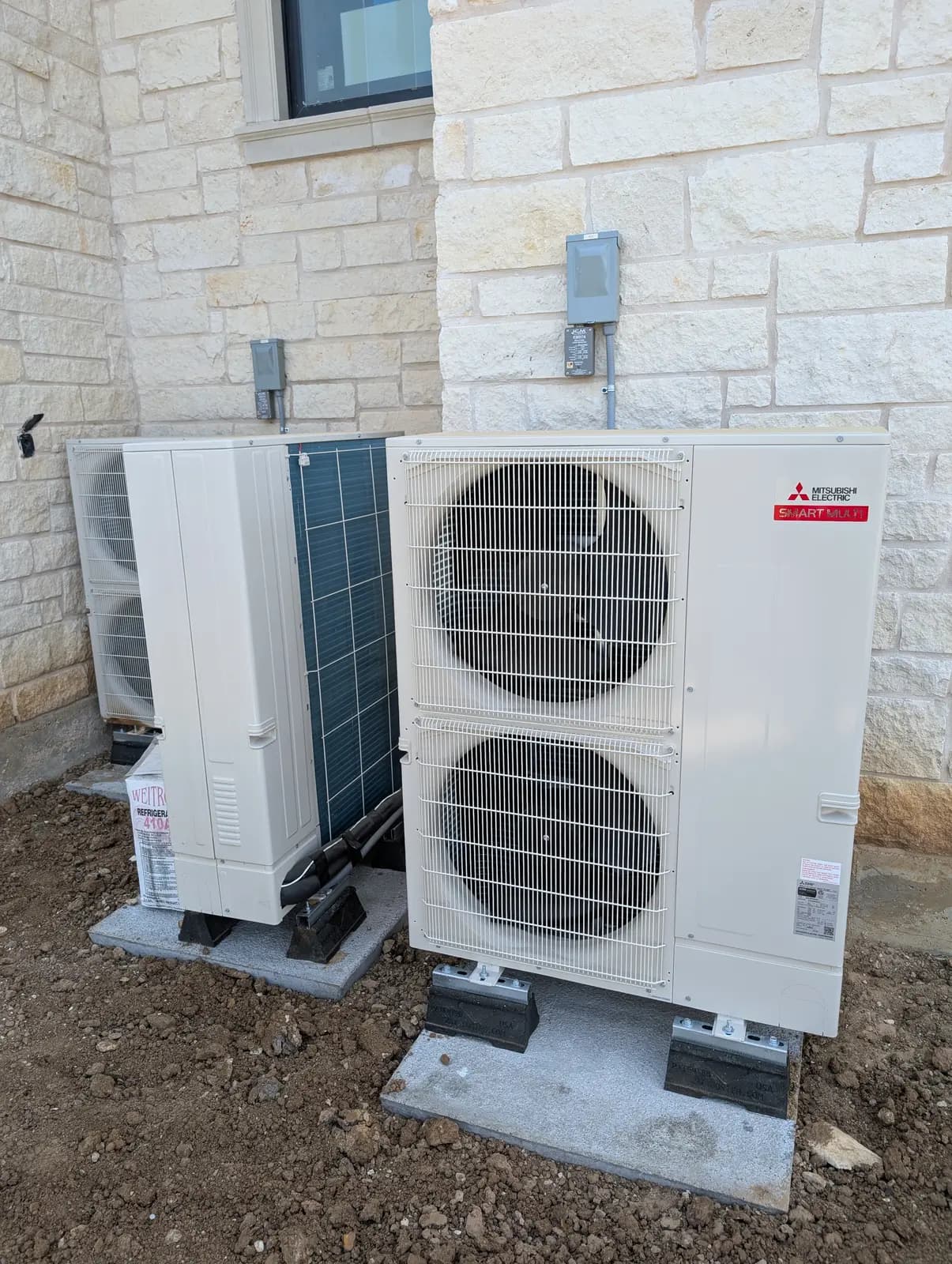 Two large Mitsubishi Electric outdoor units on pads against a limestone wall