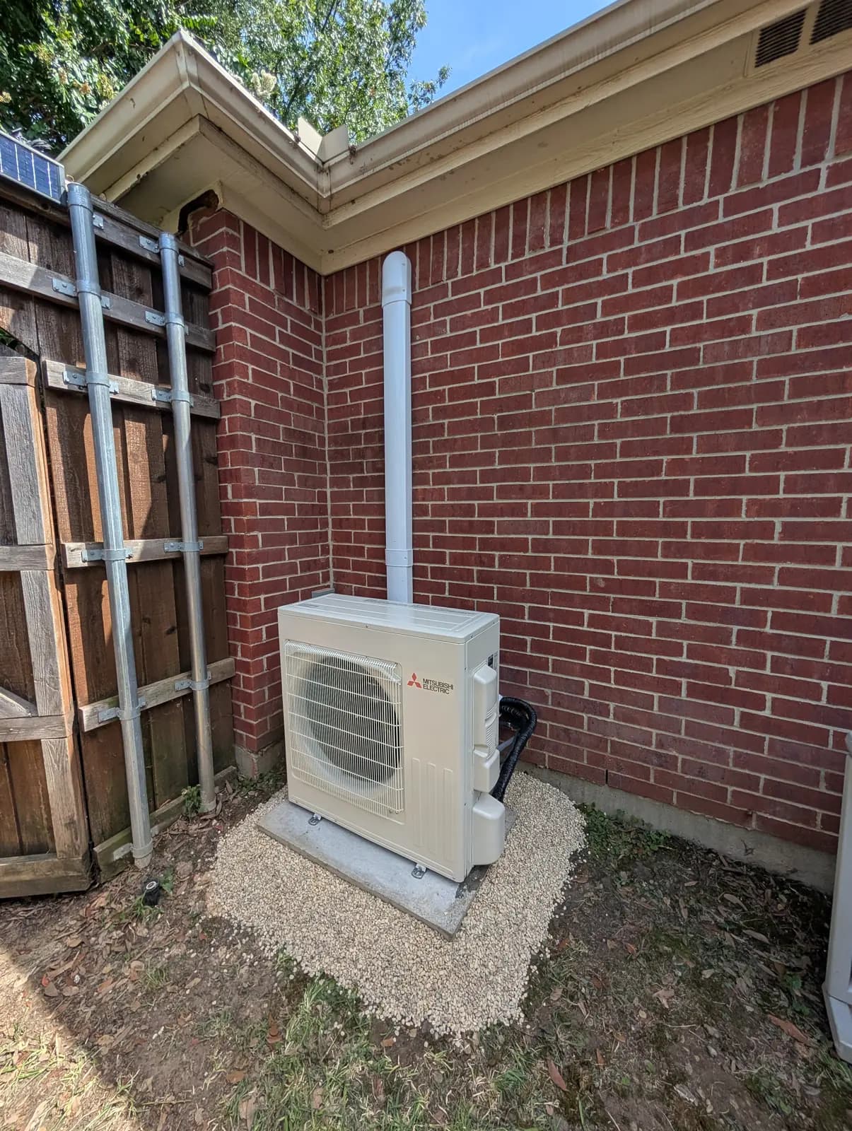 Mitsubishi outdoor unit on a gravel pad in a brick corner with a line hide running up the wall