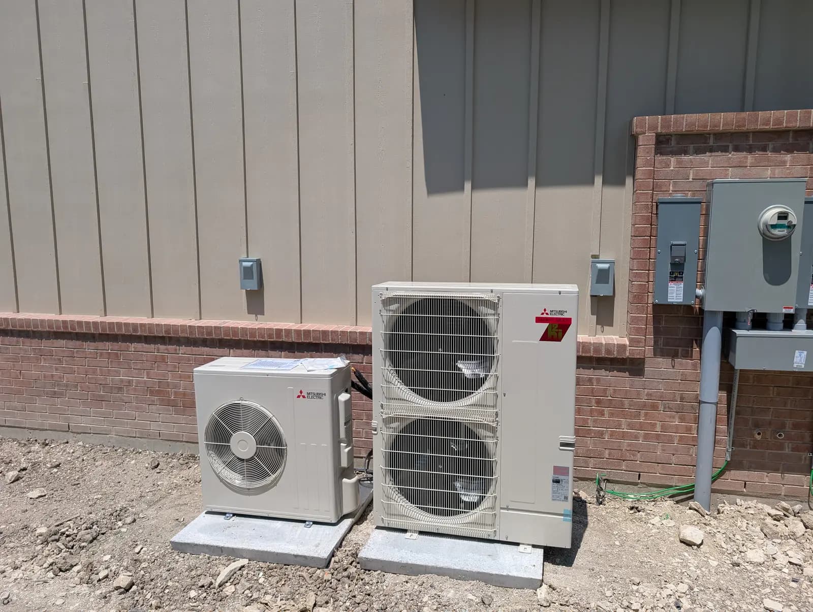 Mitsubishi single-fan and two-fan outdoor units on pads beside siding and brick