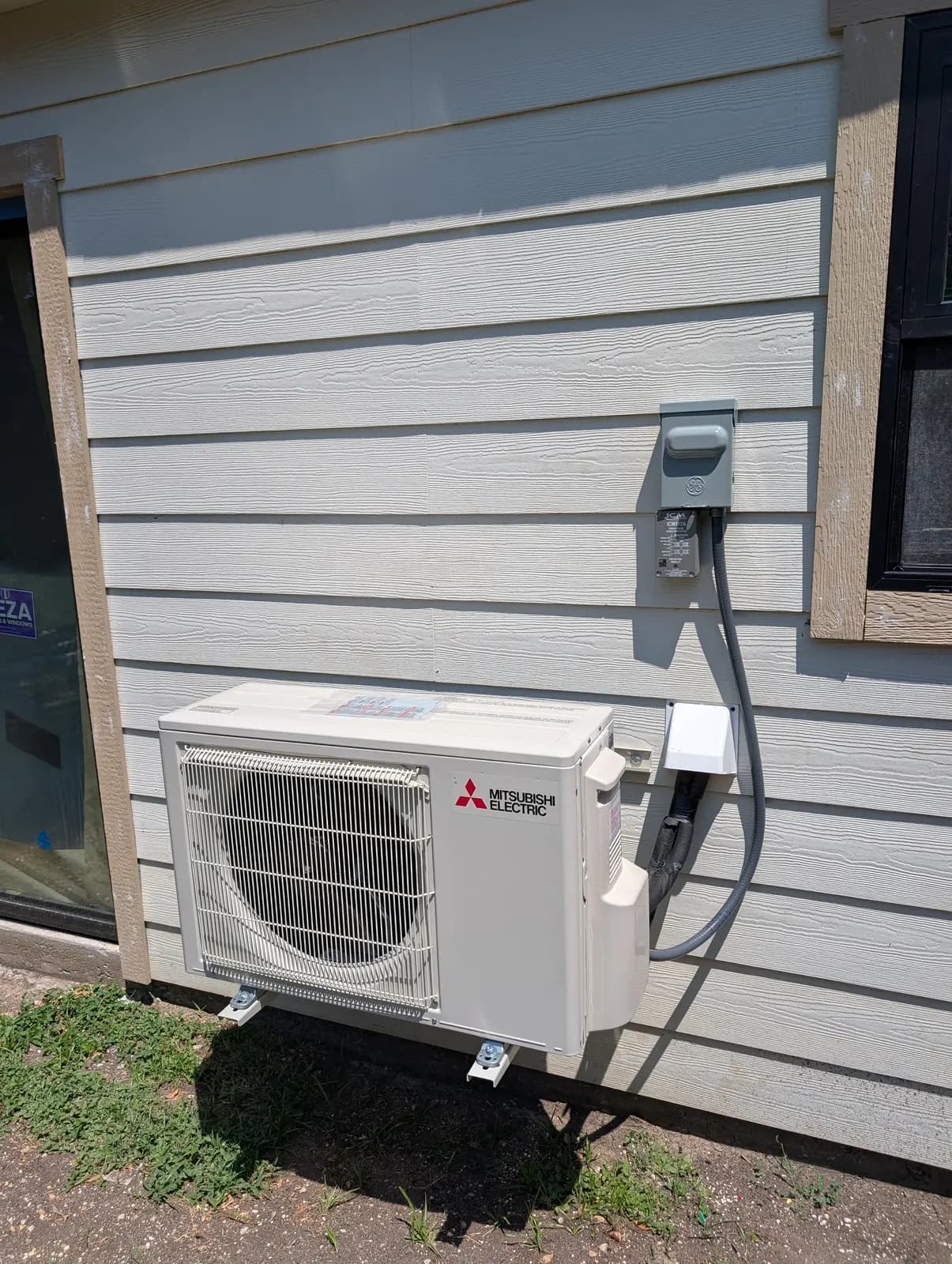 Mitsubishi Electric outdoor unit mounted on a bracket against lap siding