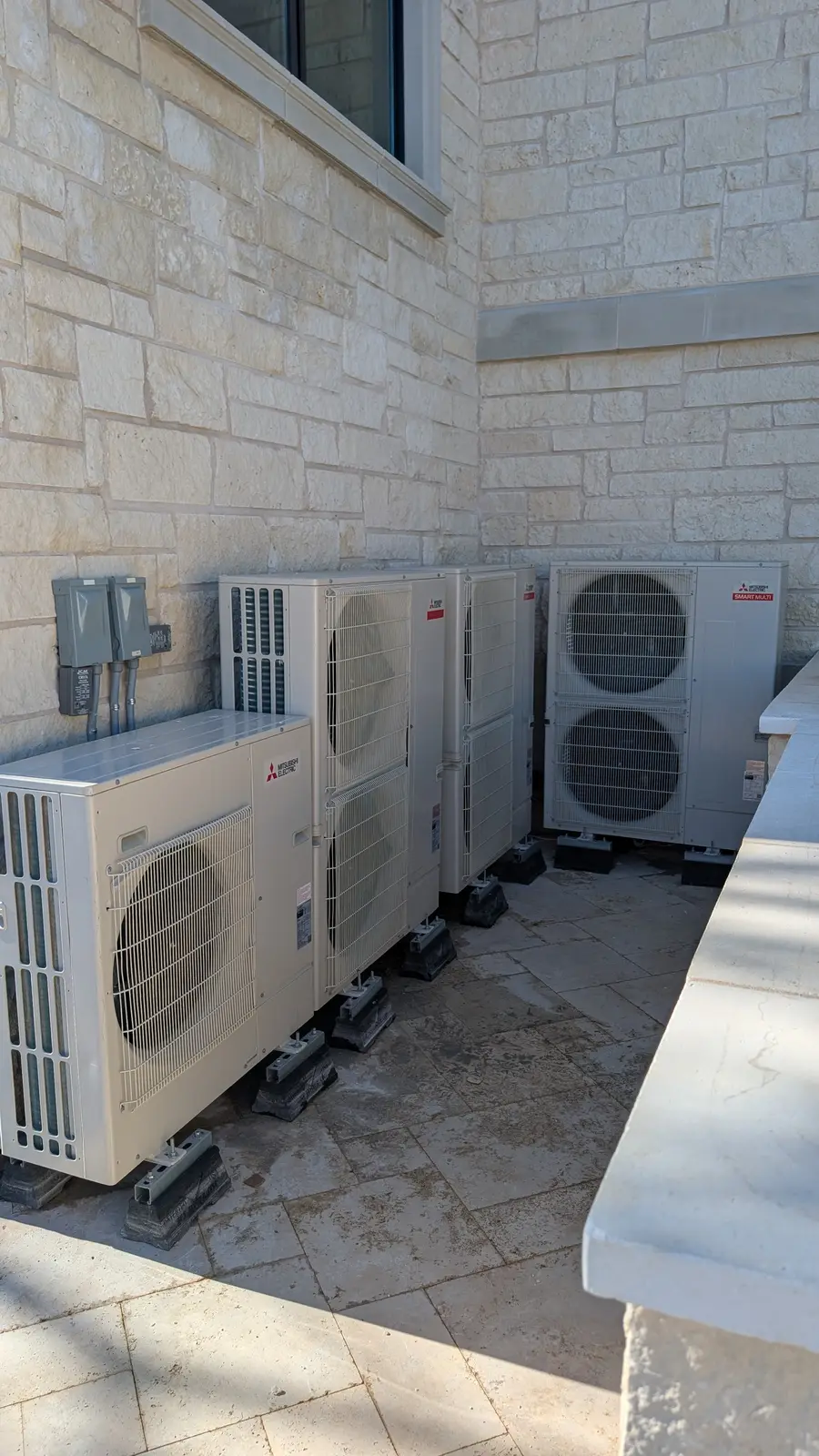 Bank of Mitsubishi outdoor units lined up along a limestone wall on a patio