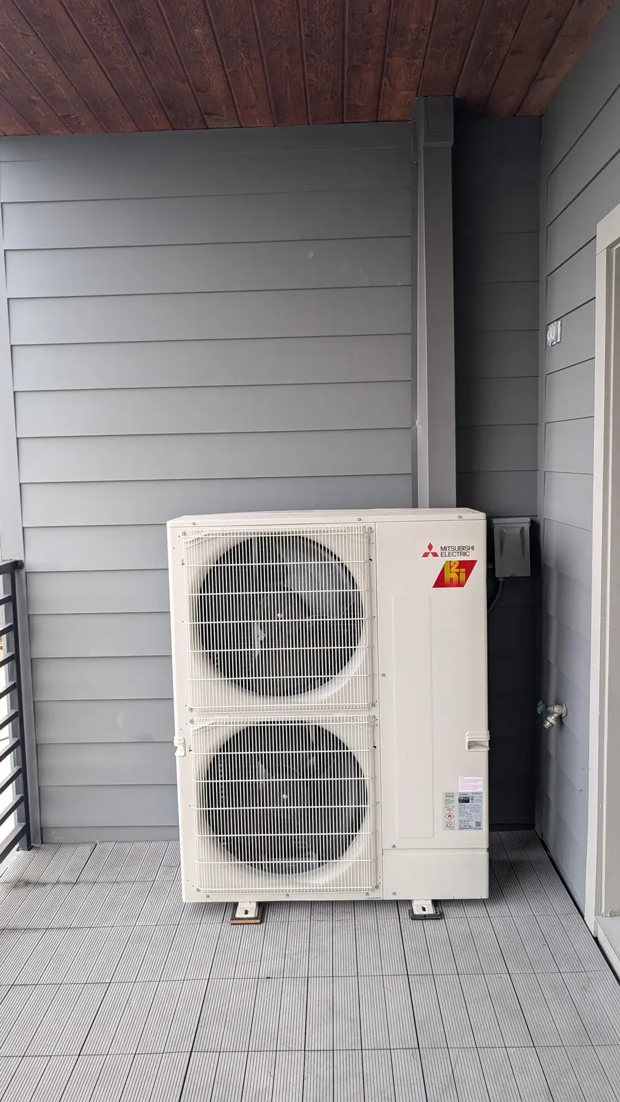 Mitsubishi Electric two-fan outdoor unit on a covered porch next to gray siding