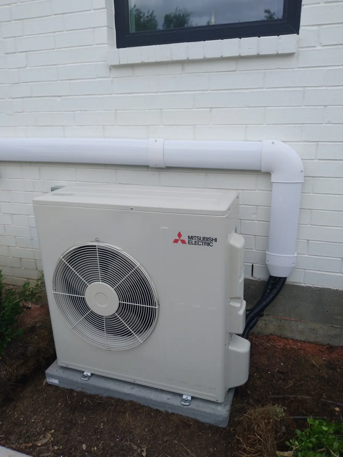 Mitsubishi Electric condenser on a pad with a white line hide cover along a painted brick wall