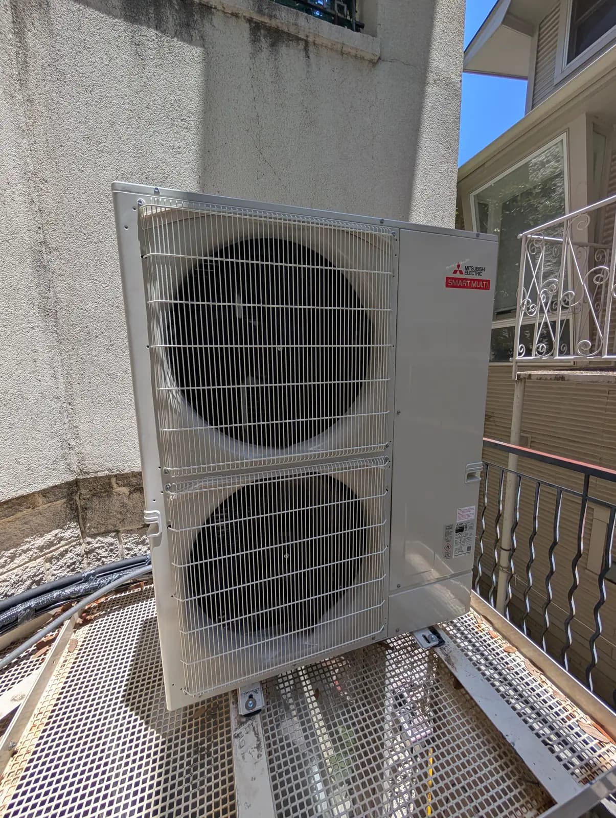 Mitsubishi Electric two-fan outdoor unit on a metal grate platform