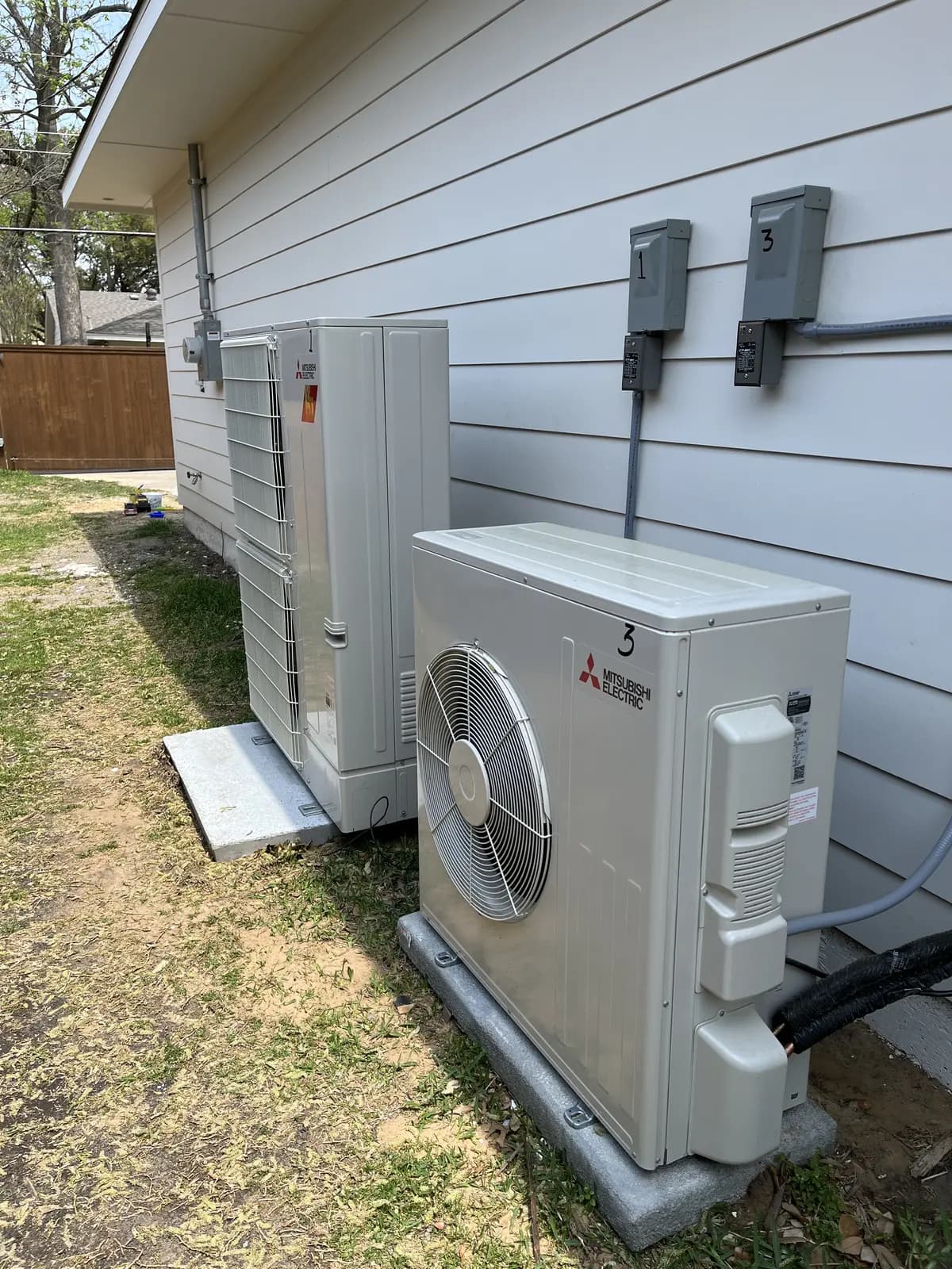 Two mini split outdoor units side by side on pads along white siding