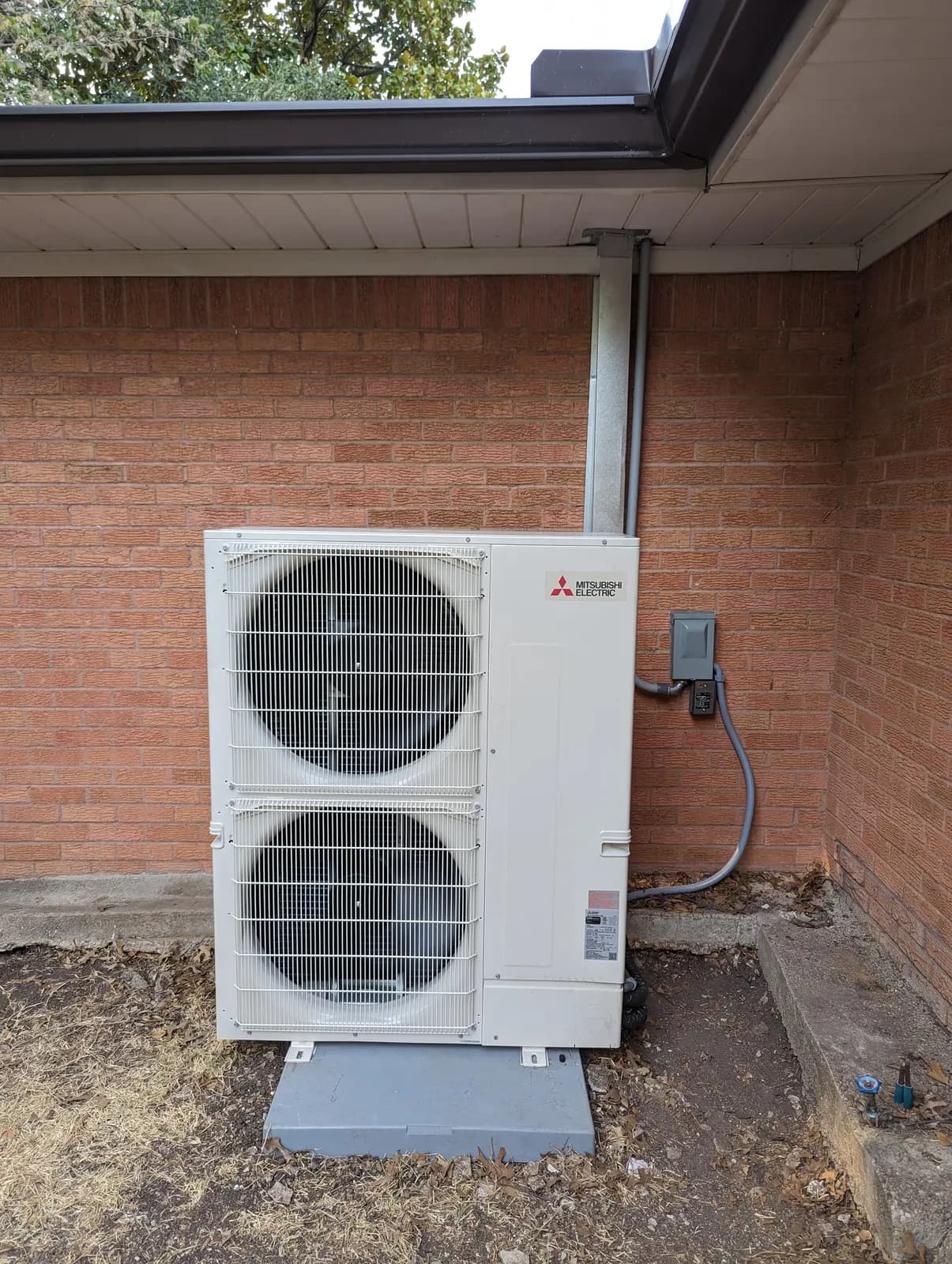 Mitsubishi Electric two-fan outdoor unit on a pad in a brick corner