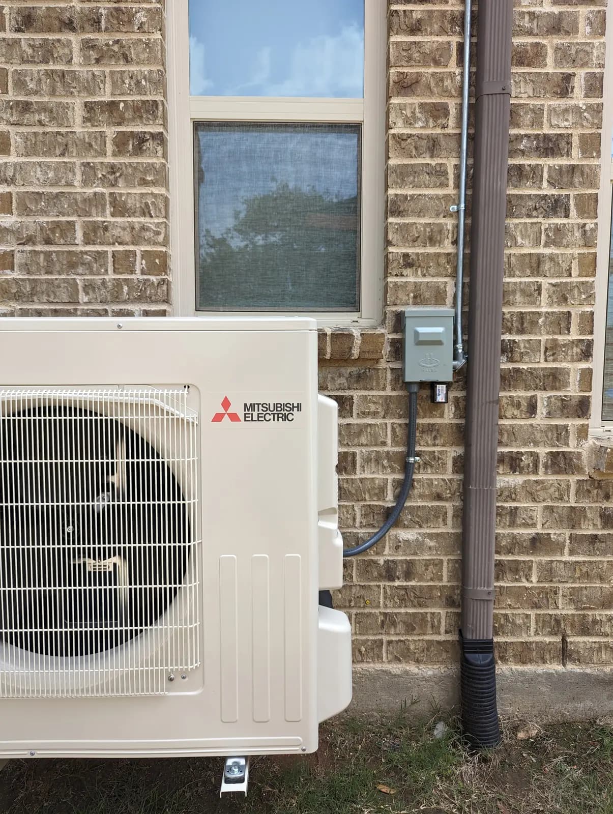 Mitsubishi Electric outdoor unit against a brick wall below a window