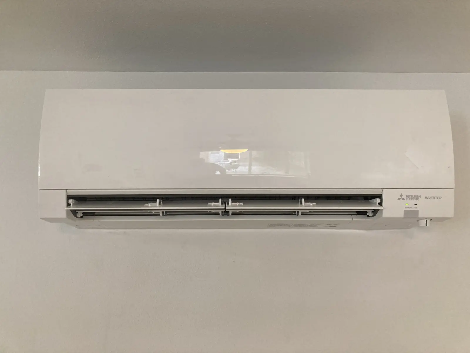 Close-up of a Mitsubishi Electric wall-mounted mini split head on a light gray wall