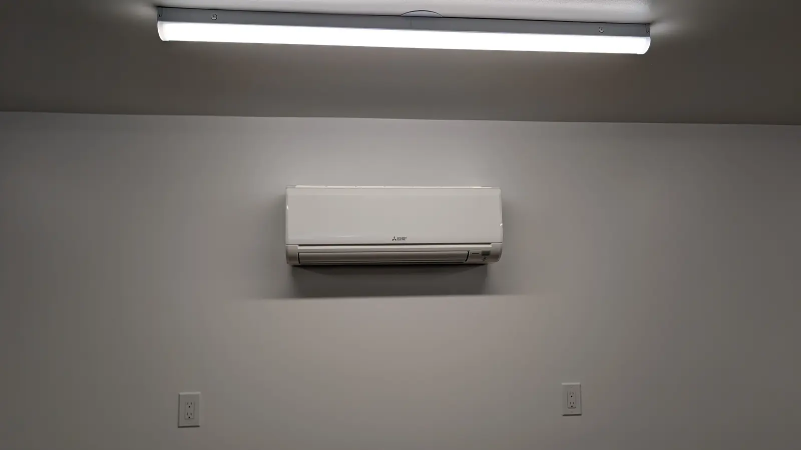 Mitsubishi wall-mount mini split centered on a gray wall under an LED light fixture