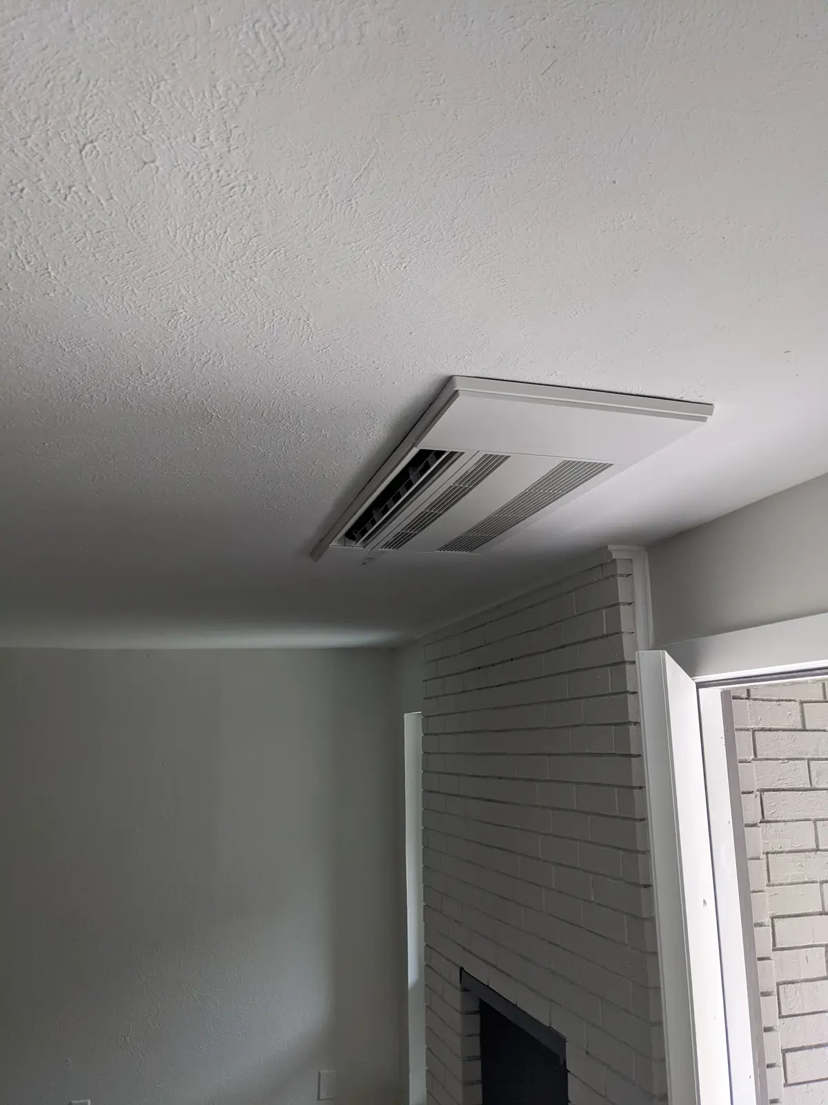 One-way ceiling cassette recessed in a textured ceiling above a painted brick fireplace