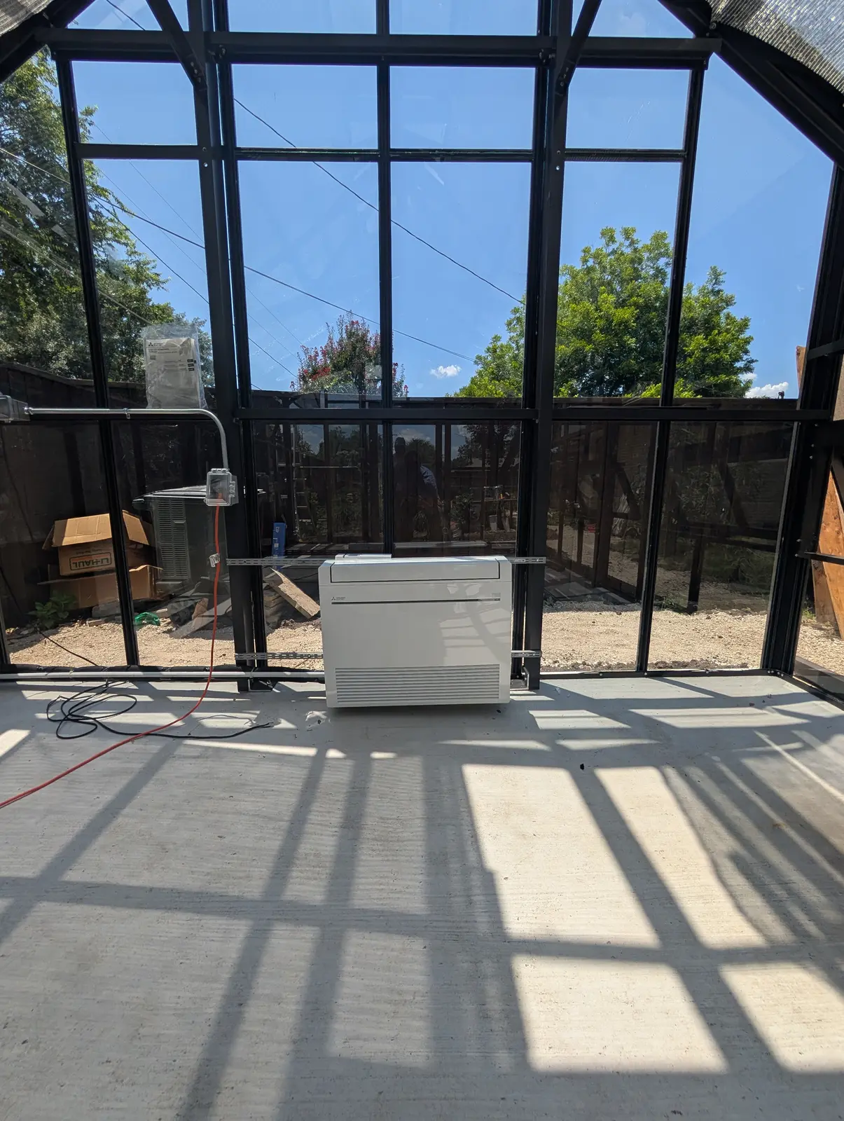 Floor-mounted mini split inside a glass-walled sunroom with sunlight on the floor