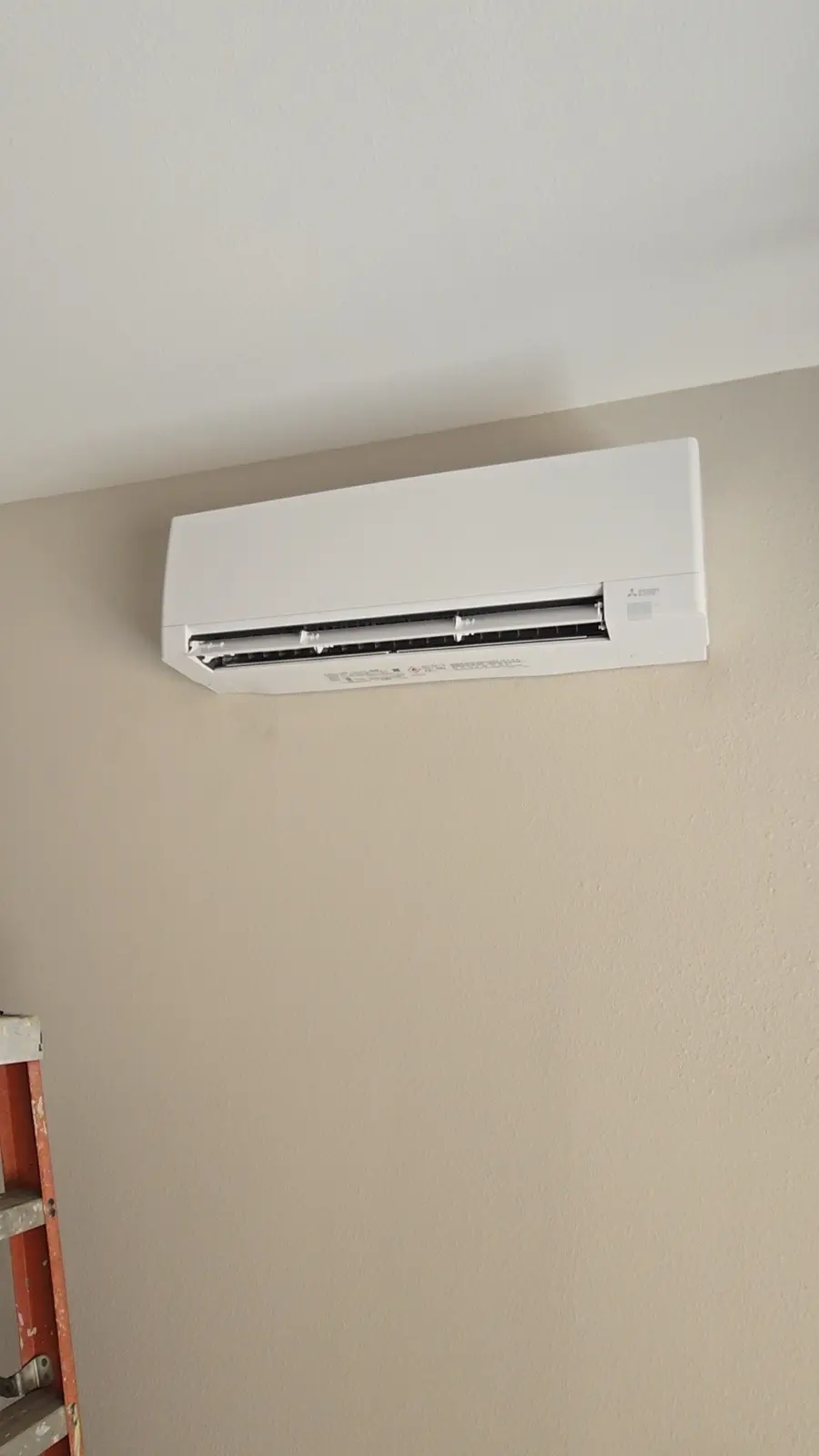 White wall-mounted mini split head installed high on a beige interior wall