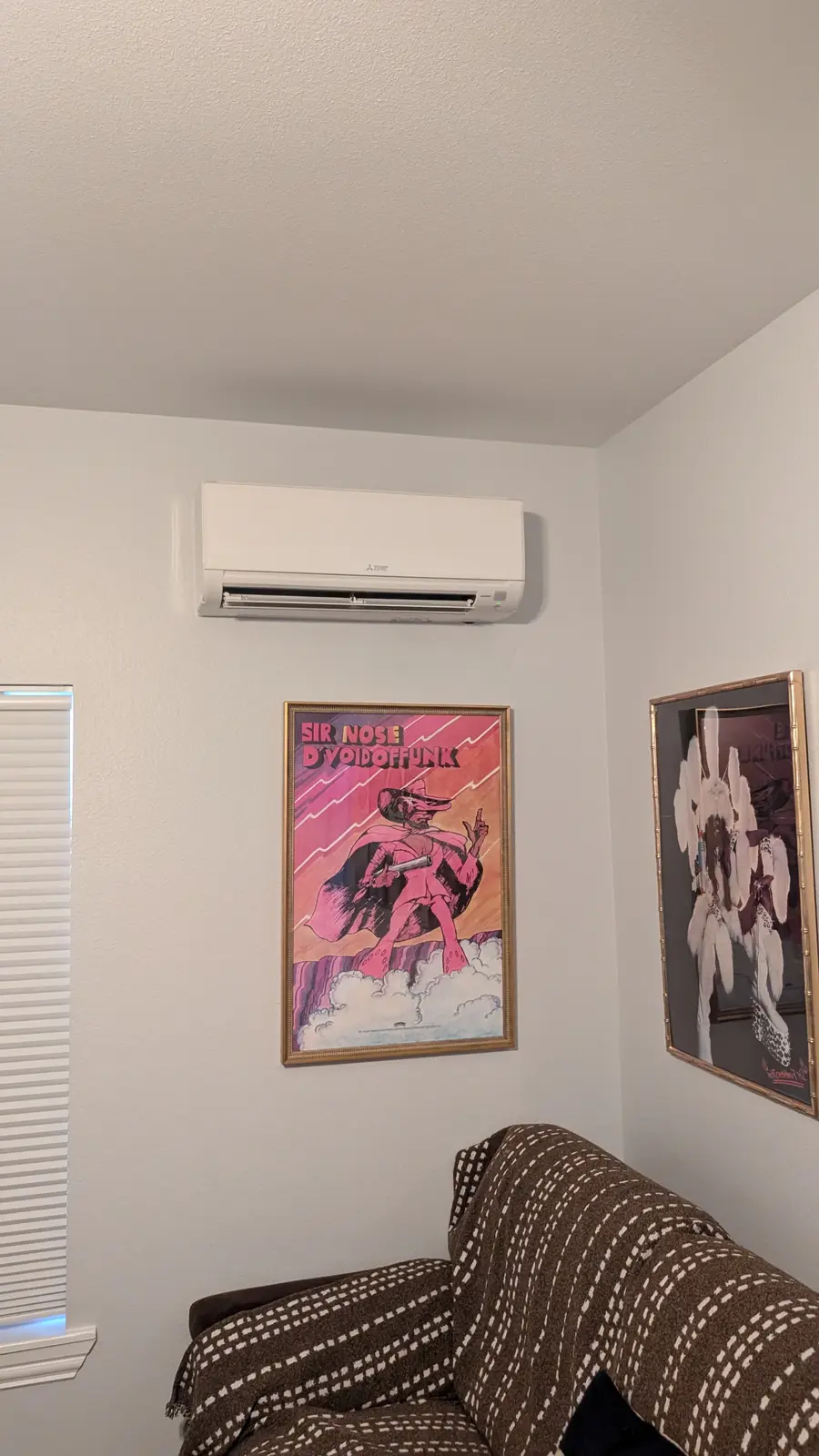 Wall-mounted mini split in a small room with framed posters and a couch