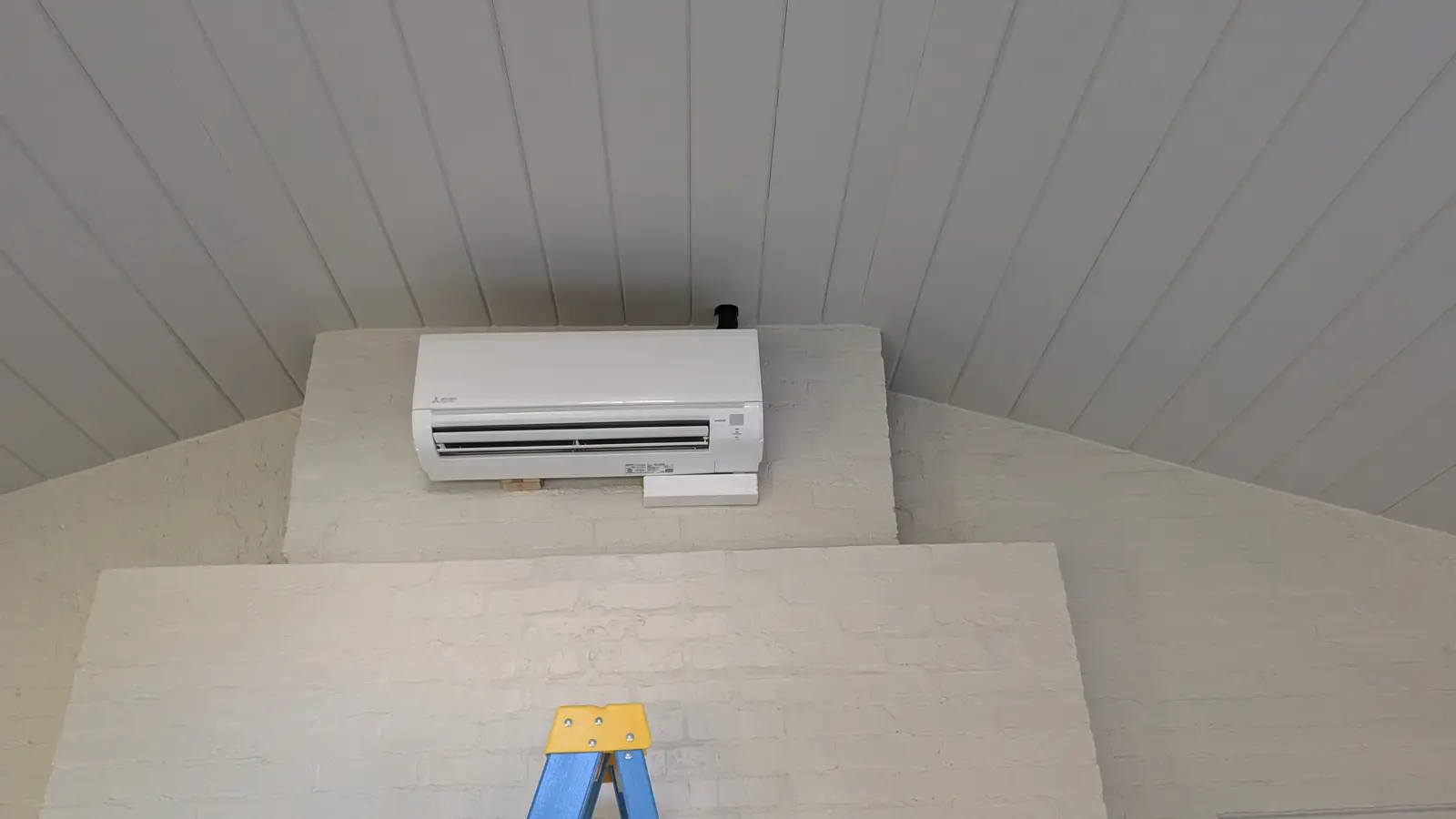 Wall-mount mini split on a painted brick bulkhead under a vaulted beadboard ceiling
