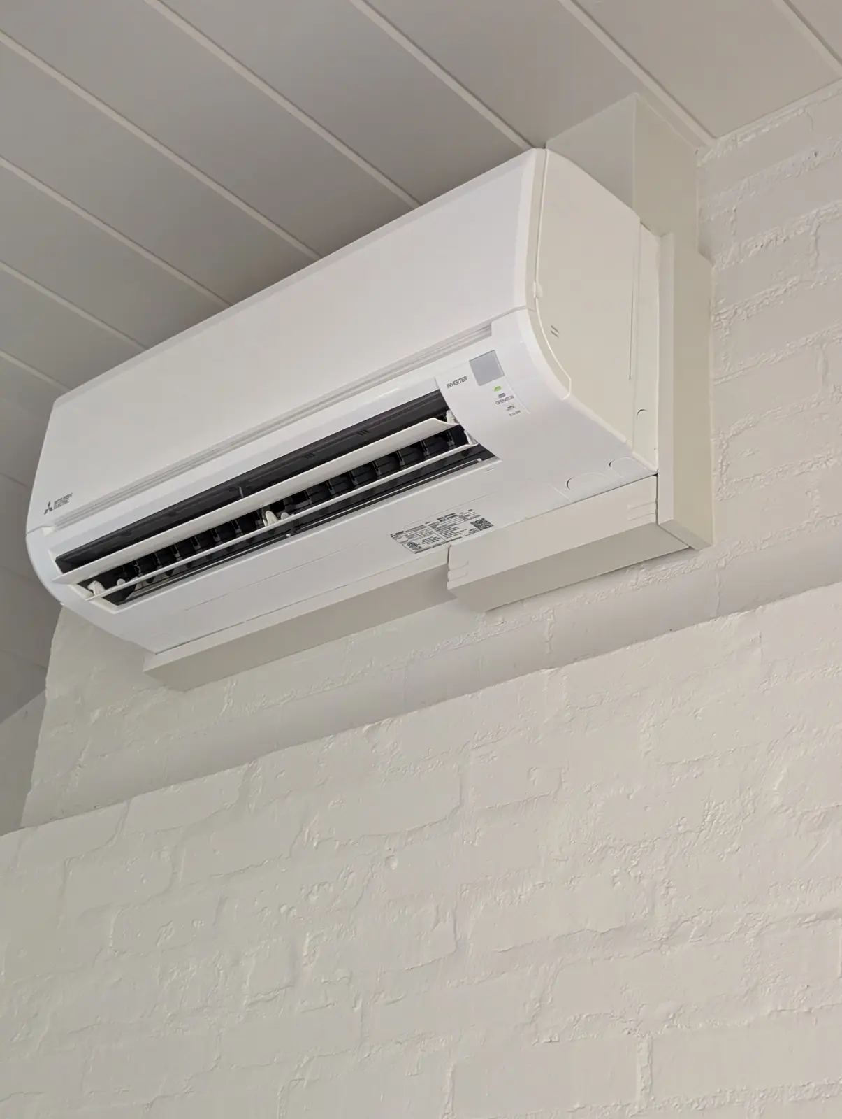 Wall-mount mini split on a white painted brick bulkhead under a beadboard ceiling