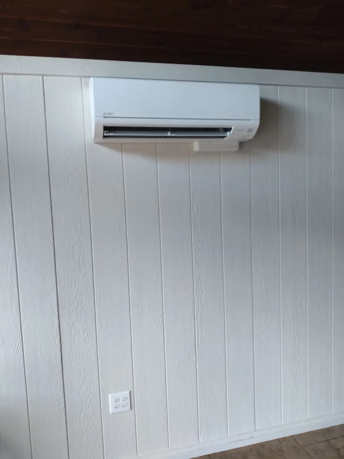 Wall-mount mini split on white vertical-panel wall beneath a dark wood ceiling