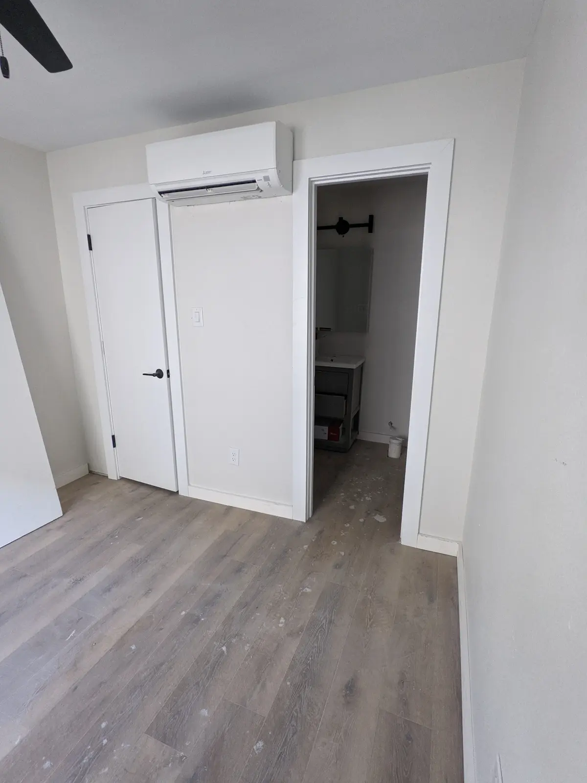 Wall-mounted mini split above a closet door in a finished room with wood-look flooring