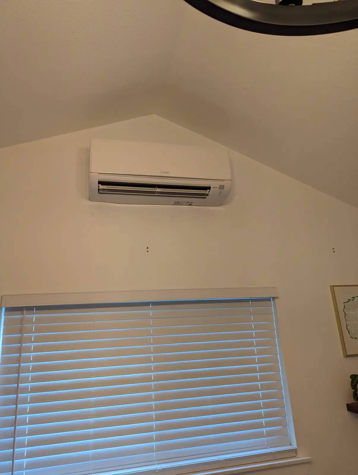 Wall-mount mini split on a vaulted wall above a window with blinds