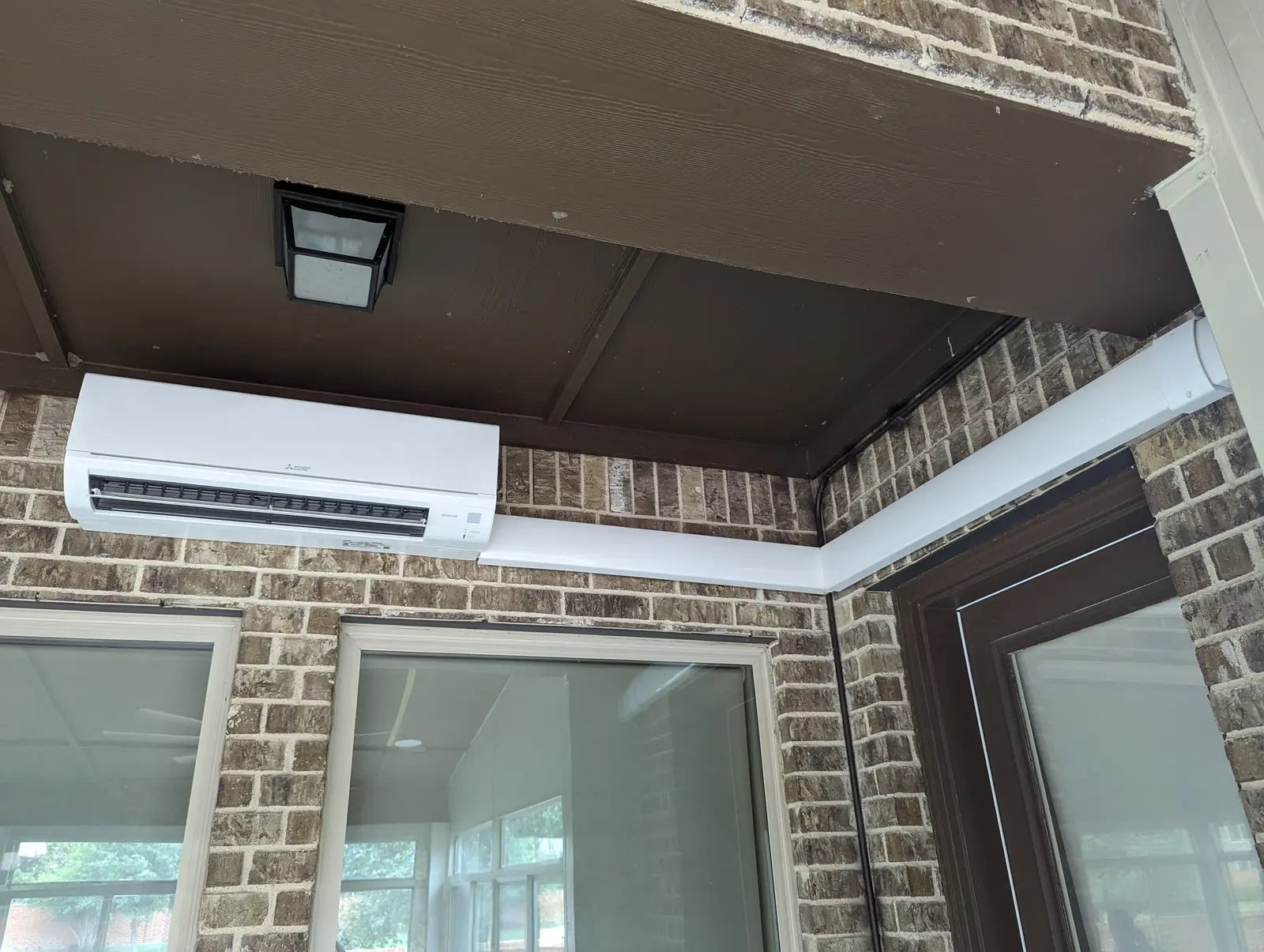 Wall-mount mini split under a covered patio ceiling above brick and windows
