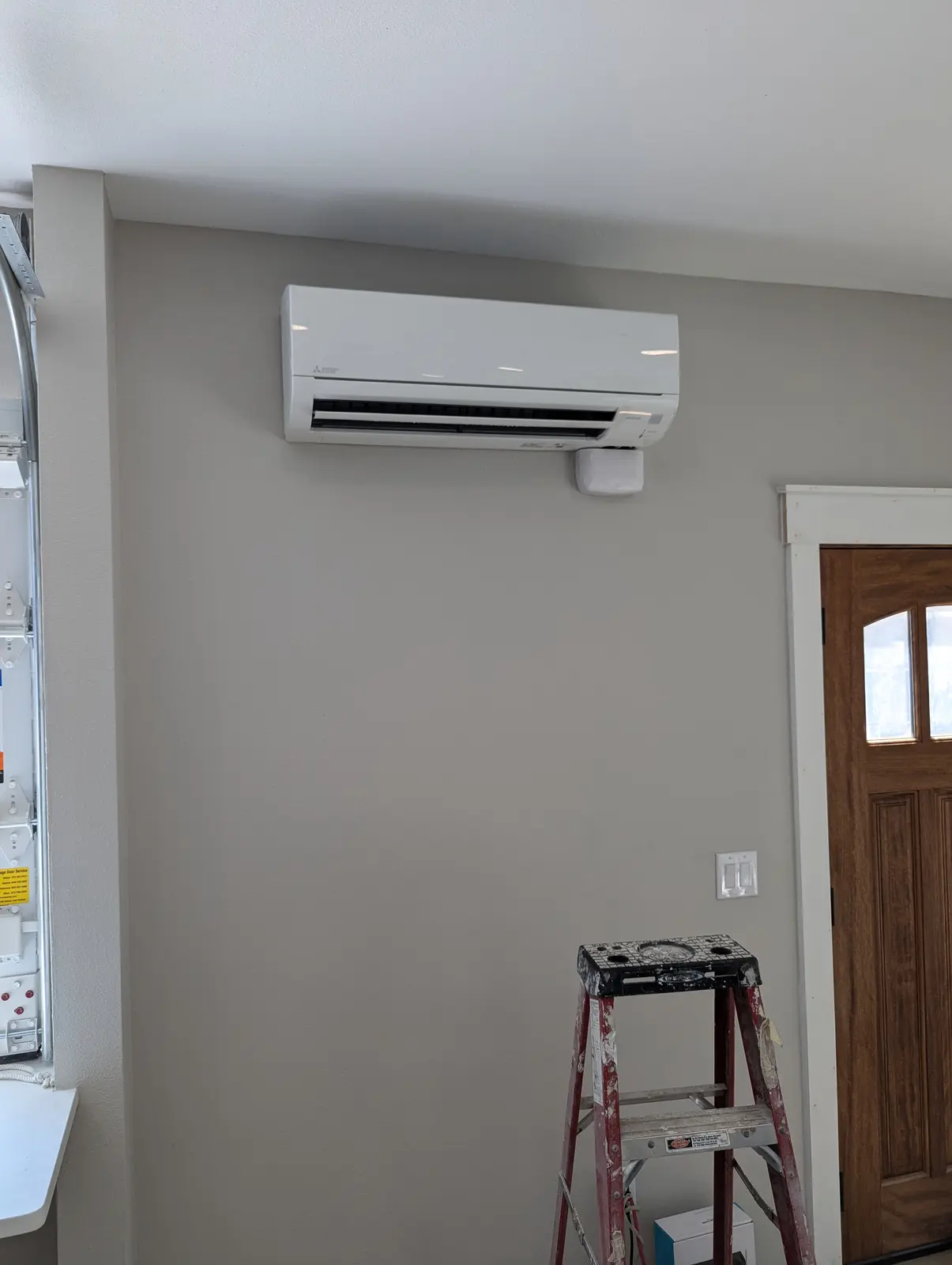 Wall-mounted mini split above a light switch near a wood entry door