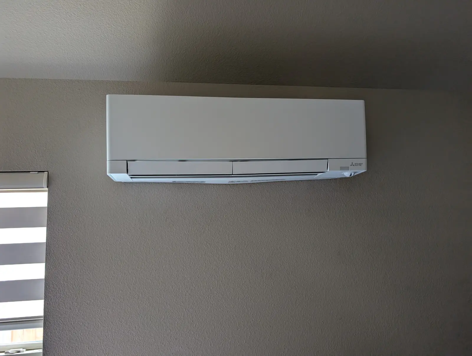 Wall-mounted mini split head high on a taupe interior wall
