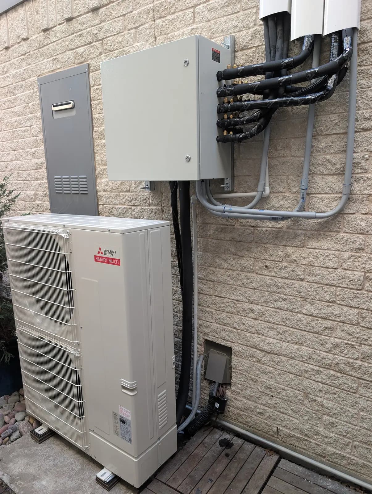 Mitsubishi multi-zone outdoor unit with branch box and line hides on a brick wall