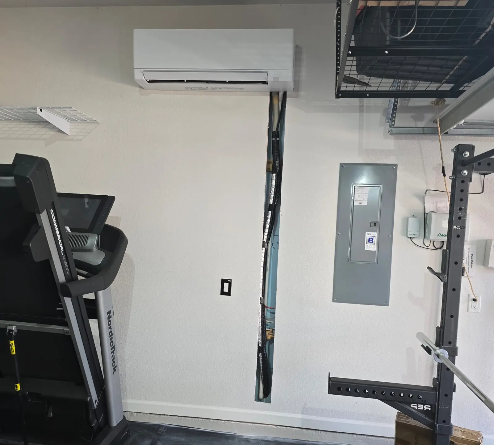 Wall-mount mini split in a garage home gym with storage racks and a treadmill