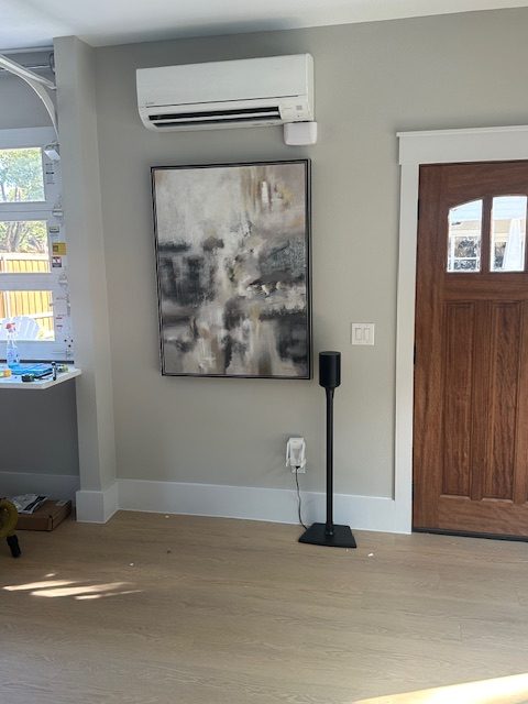 Wall-mounted mini split unit installed above abstract artwork near wooden door.