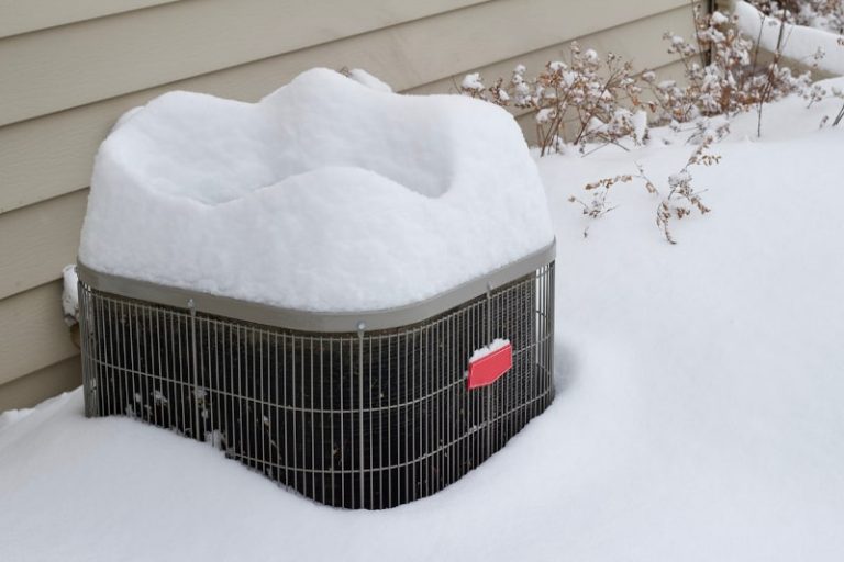 An outdoor heat pump unit covered in snow during winter.