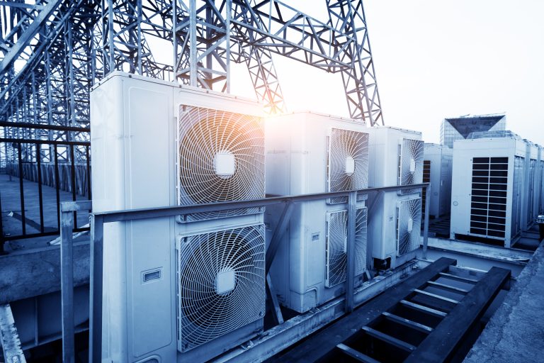 A row of industrial HVAC units on a rooftop with metal structures and the sun shining in the background