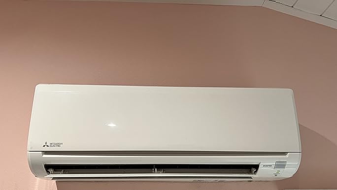 Mitsubishi Electric MSZ-HM15NA wall-mounted indoor air conditioning unit installed on a pink wall.