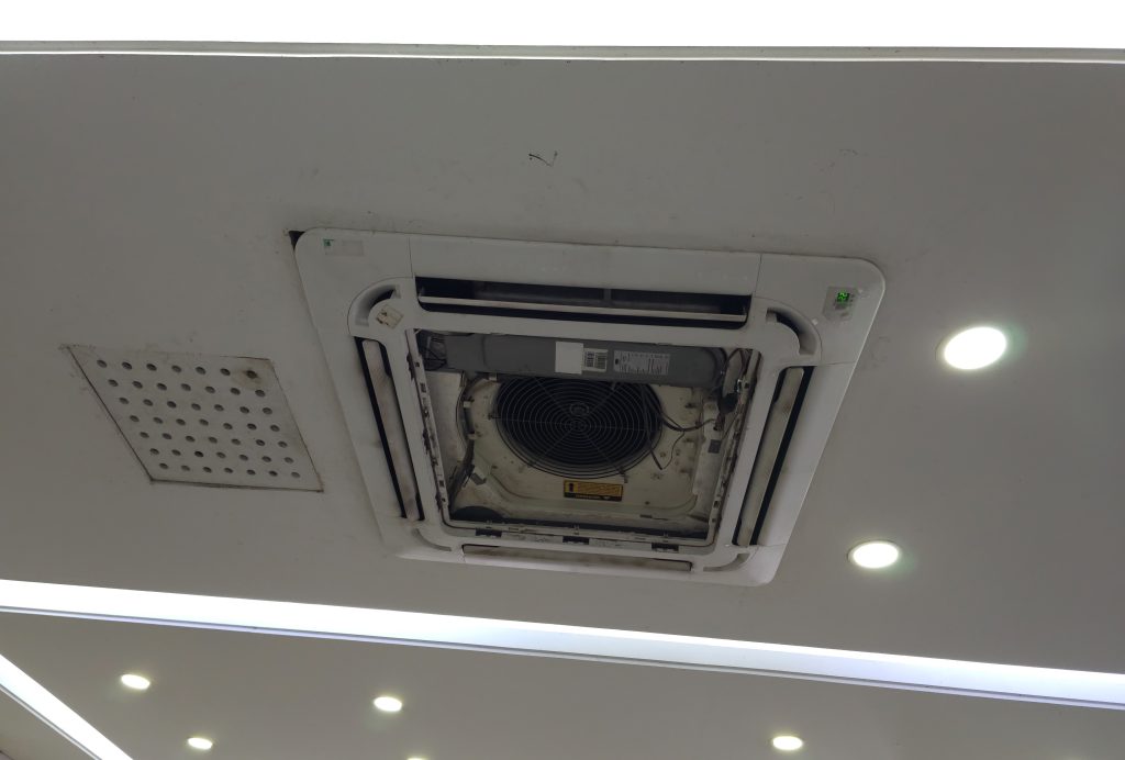 A close-up of a ceiling cassette air conditioning unit with its interior components exposed for maintenance or repair.