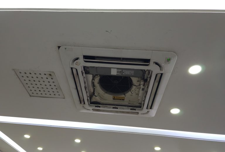 A close-up of a ceiling cassette air conditioning unit with its interior components exposed for maintenance or repair.