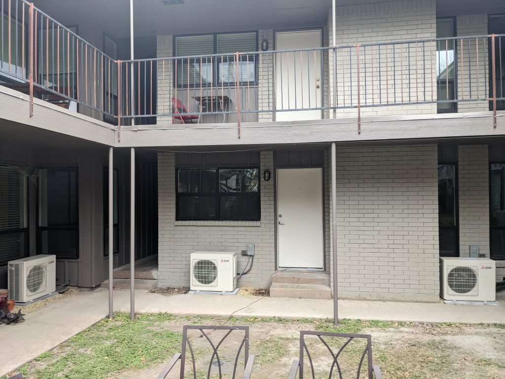 Two-story apartment building with white doors, balconies, and outdoor AC units
